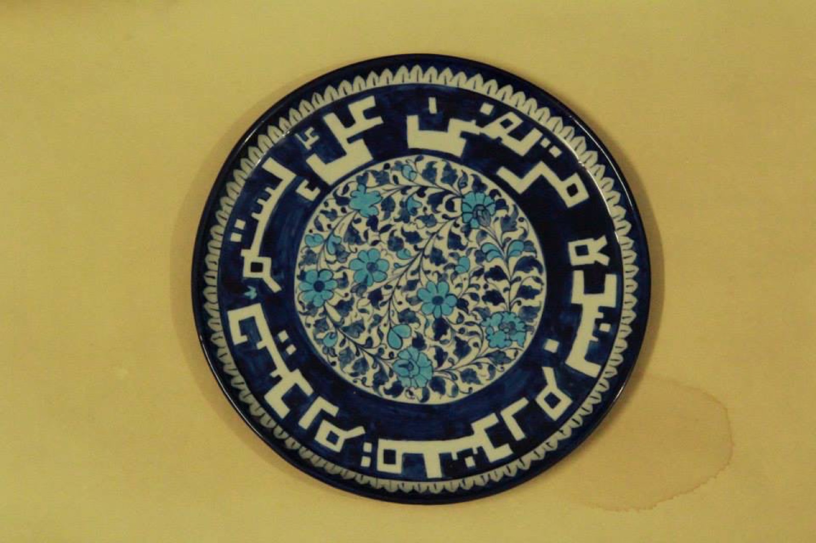 Blue and white Iznik-style plate with floral centre and kufic border